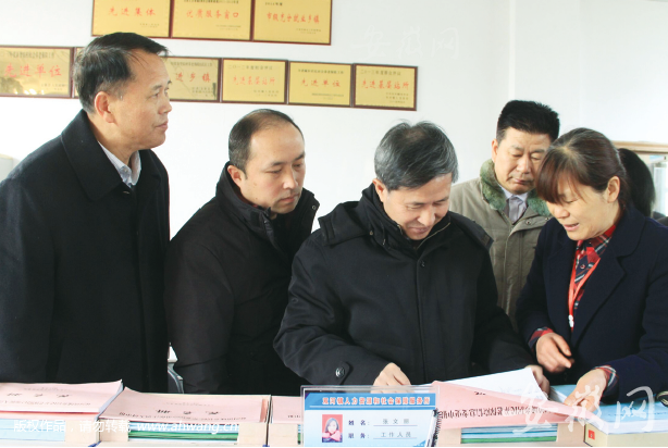 國家人社部農保司司長劉從龍在金寨縣雙河鎮社保所檢查社保扶貧工作。圖為劉司長（左三）查看扶貧代繳臺賬。